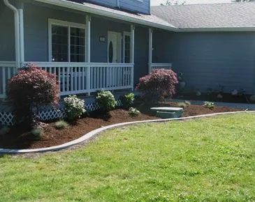 A blue house with a porch and a lush green lawn in front of it.