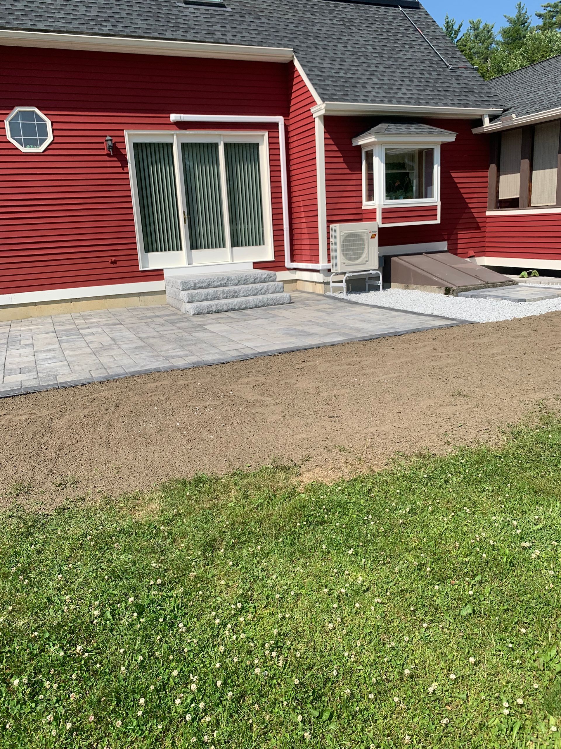 Red house with patio pavers, steps, and sliding glass doors. Brown dirt and green grass in the foreground.
