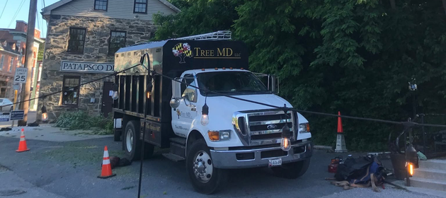 White dump truck parked by stone building at dusk, with traffic cones and a worker near the rear.
