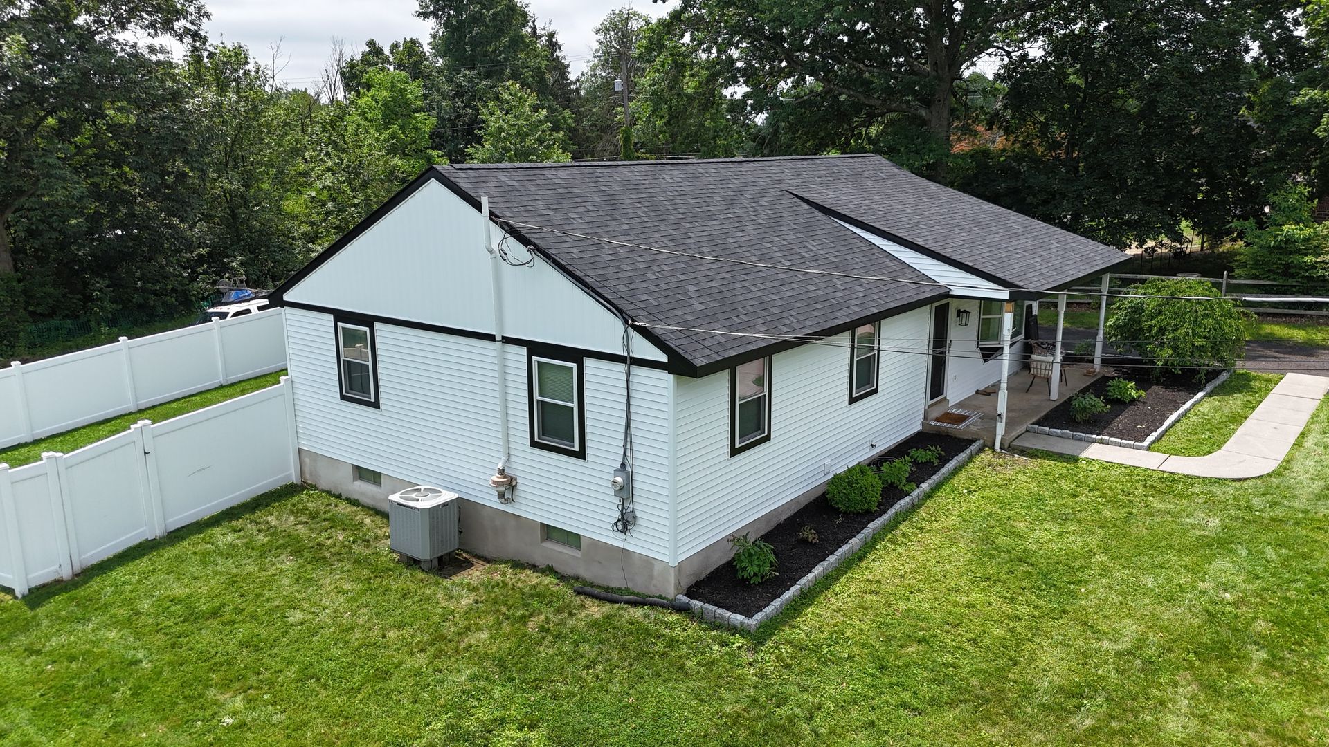 White house with black roof, landscaping, and a white fence on a grassy lawn.