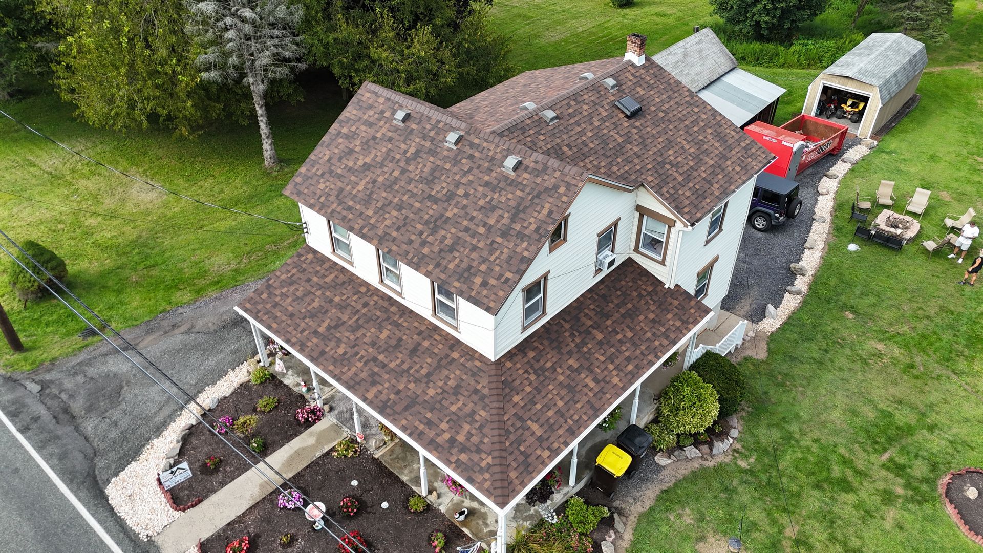 Overhead view of a two-story white house with brown roof, porch, driveway, and landscaping.