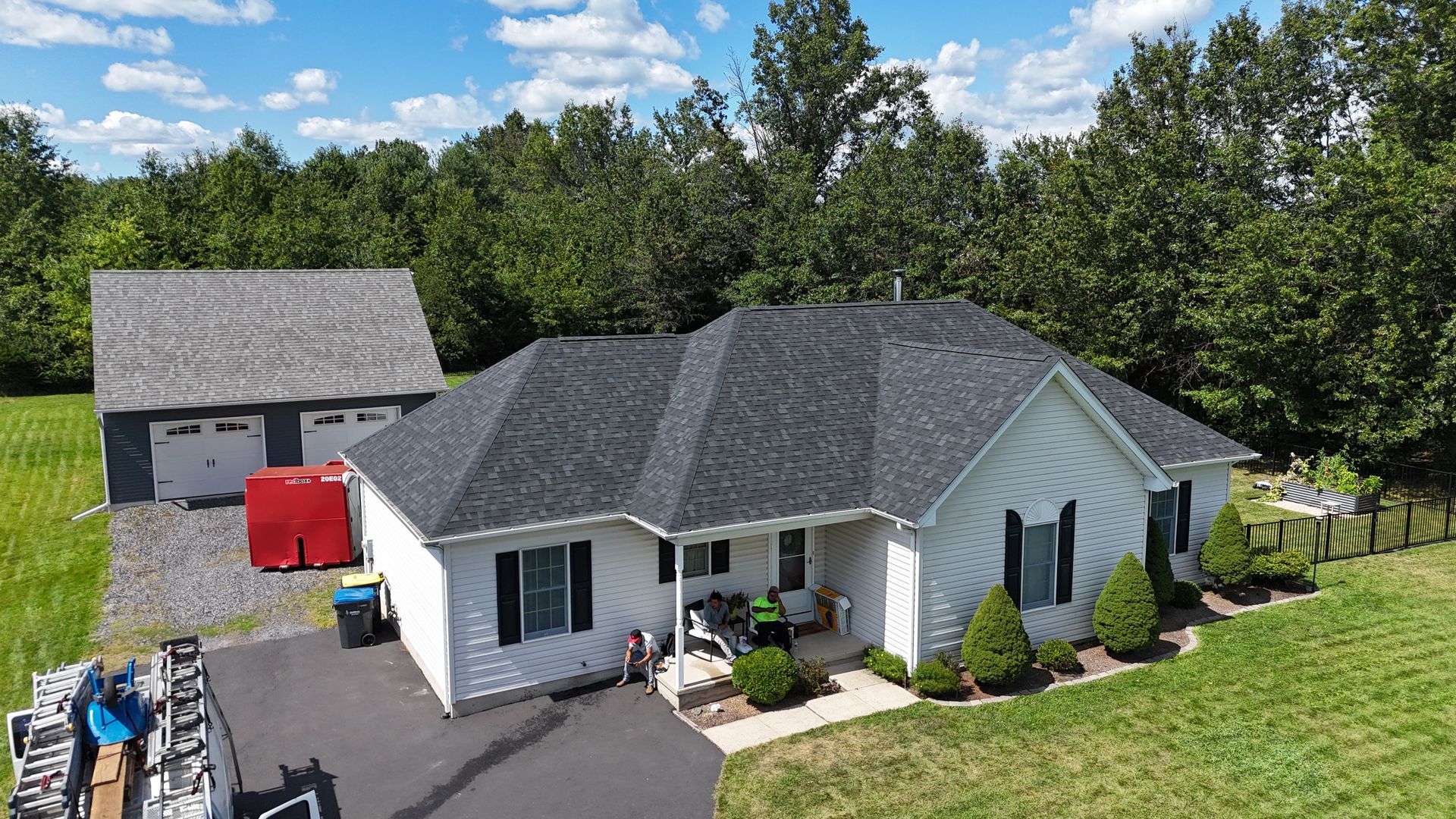 White house with black roof and detached garage on a green lawn. Sunny day.