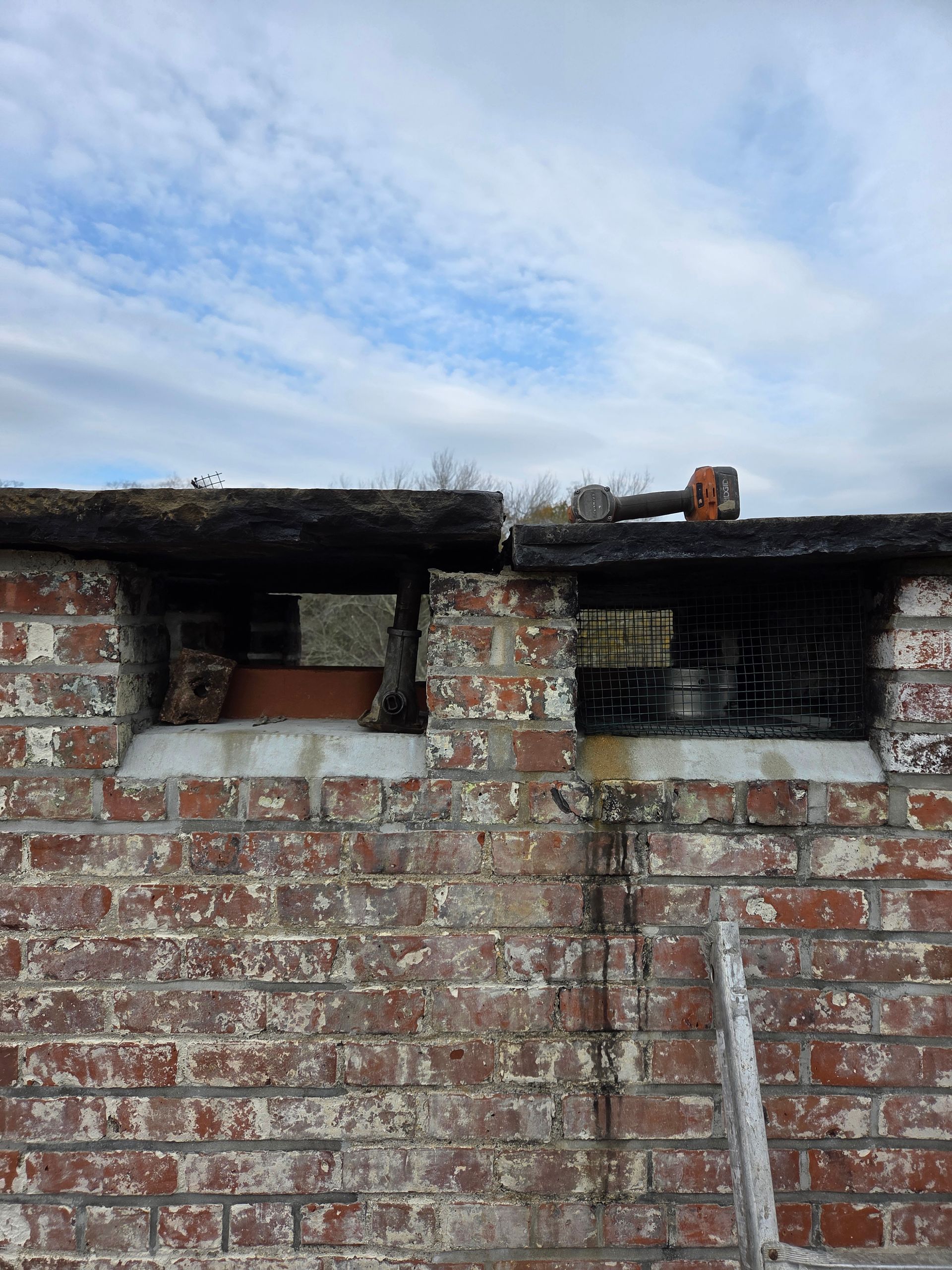 Brick chimney with two openings, a tool rests on top, and a cloudy sky above.