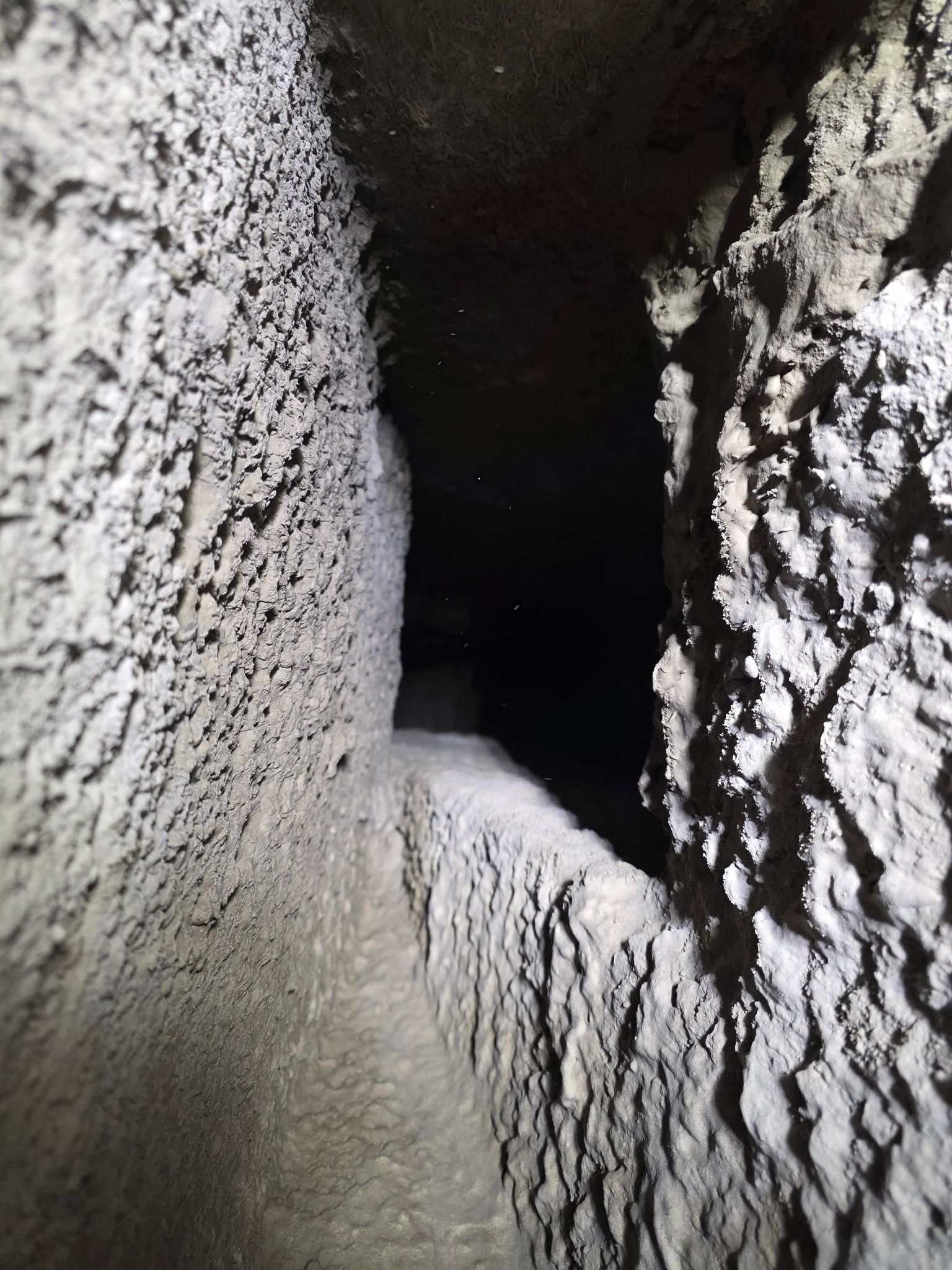 Narrow, dark, rectangular tunnel with textured, gray walls the tunnel recedes into darkness.