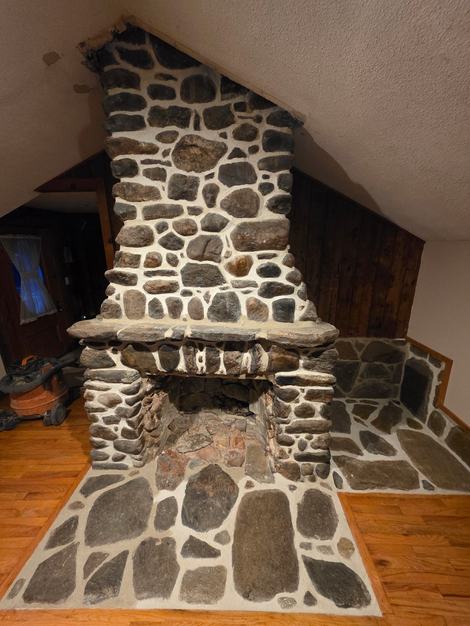 Stone fireplace with a hearth, chimney, and wooden floor in a sloped-ceiling room.