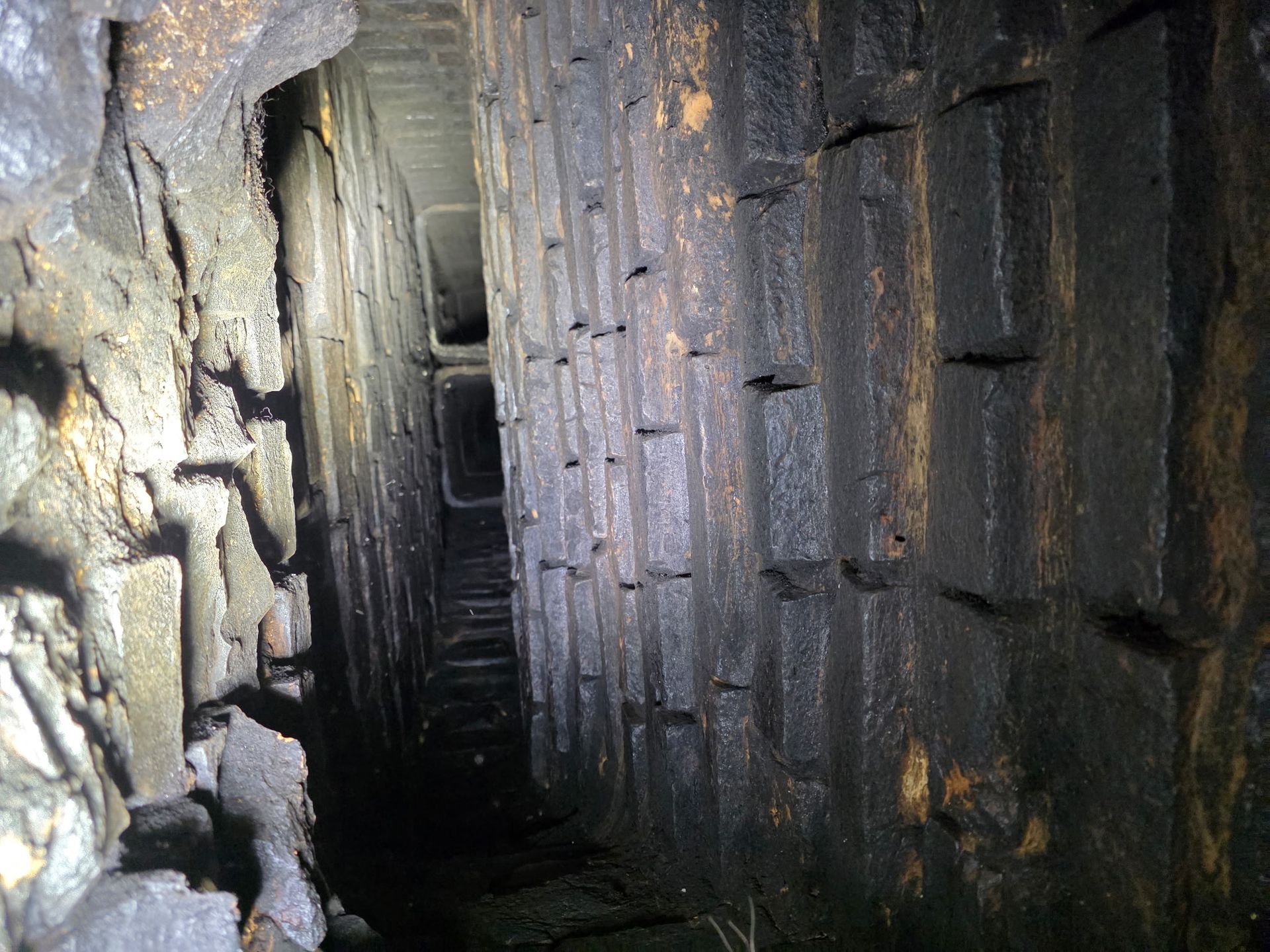 Narrow, dark tunnel with brick walls, leading to an obscured opening.
