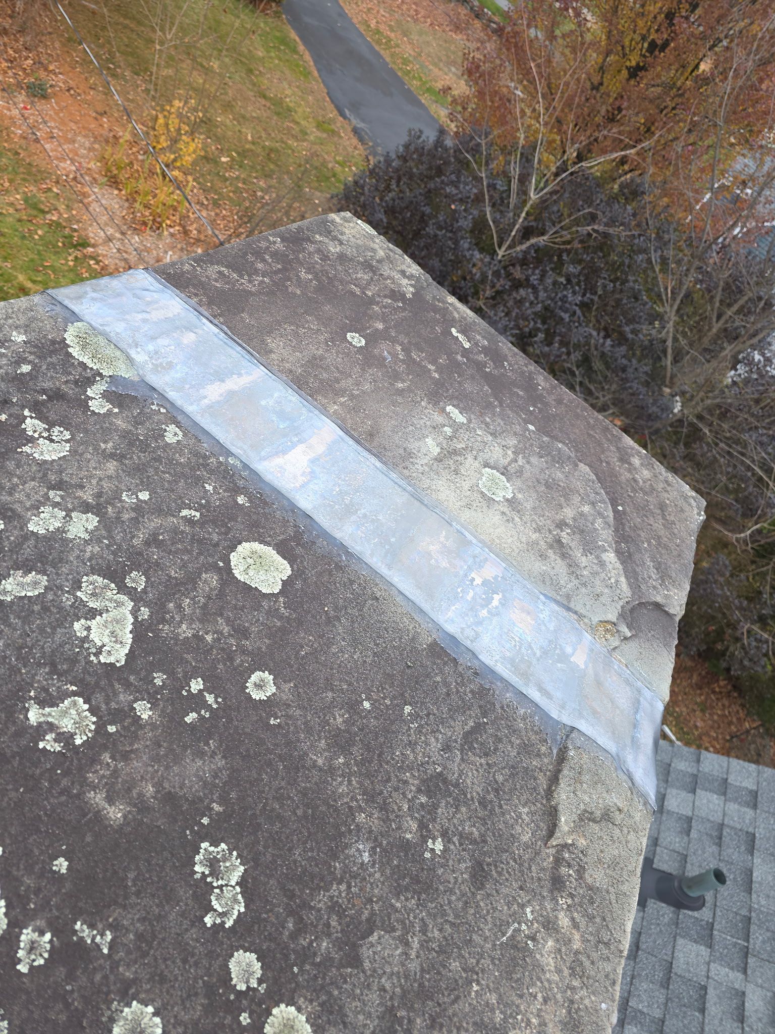 Close-up view of a dark gray roof with patches of lichen and a silver metal flashing strip asphalt shingles visible on the lower roof.