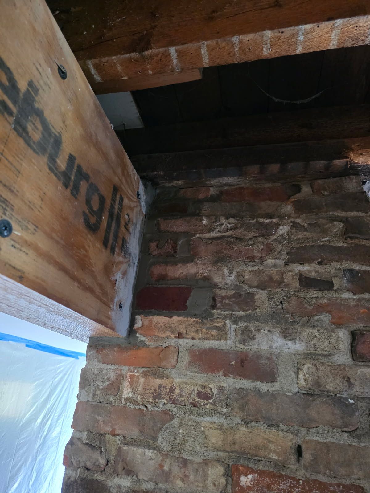 Interior brick chimney in an attic with exposed masonry and wooden roof framing.