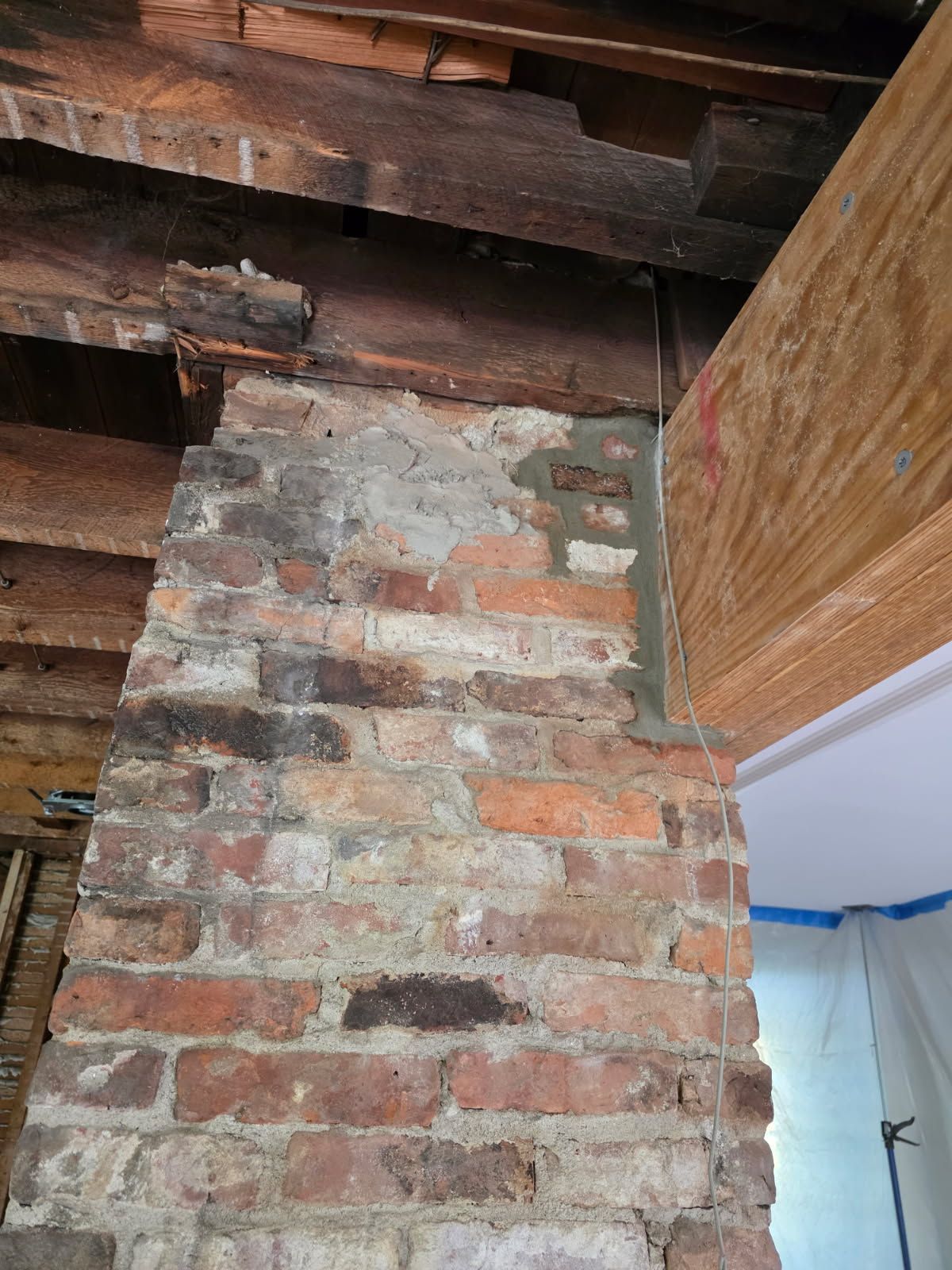 Interior view of a brick chimney in an attic with visible mortar deterioration.