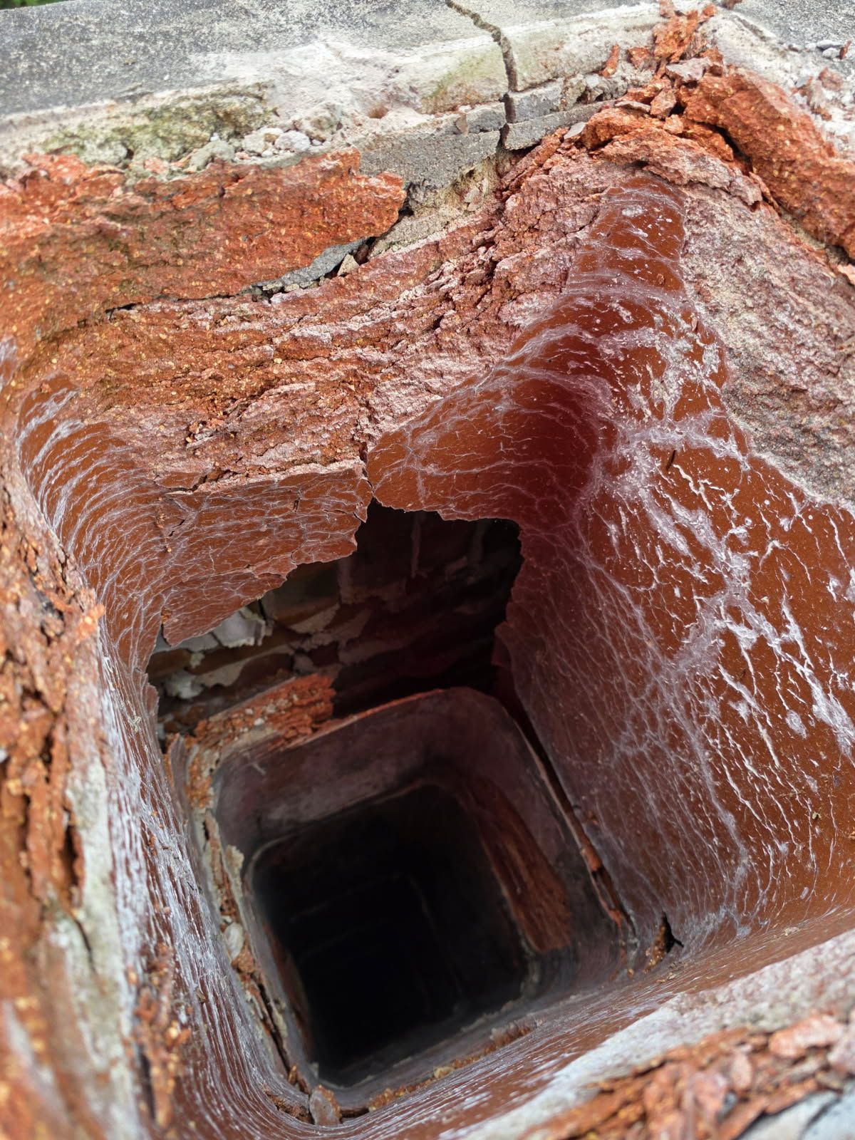 View looking down inside a brick chimney flue showing soot buildup and interior masonry.