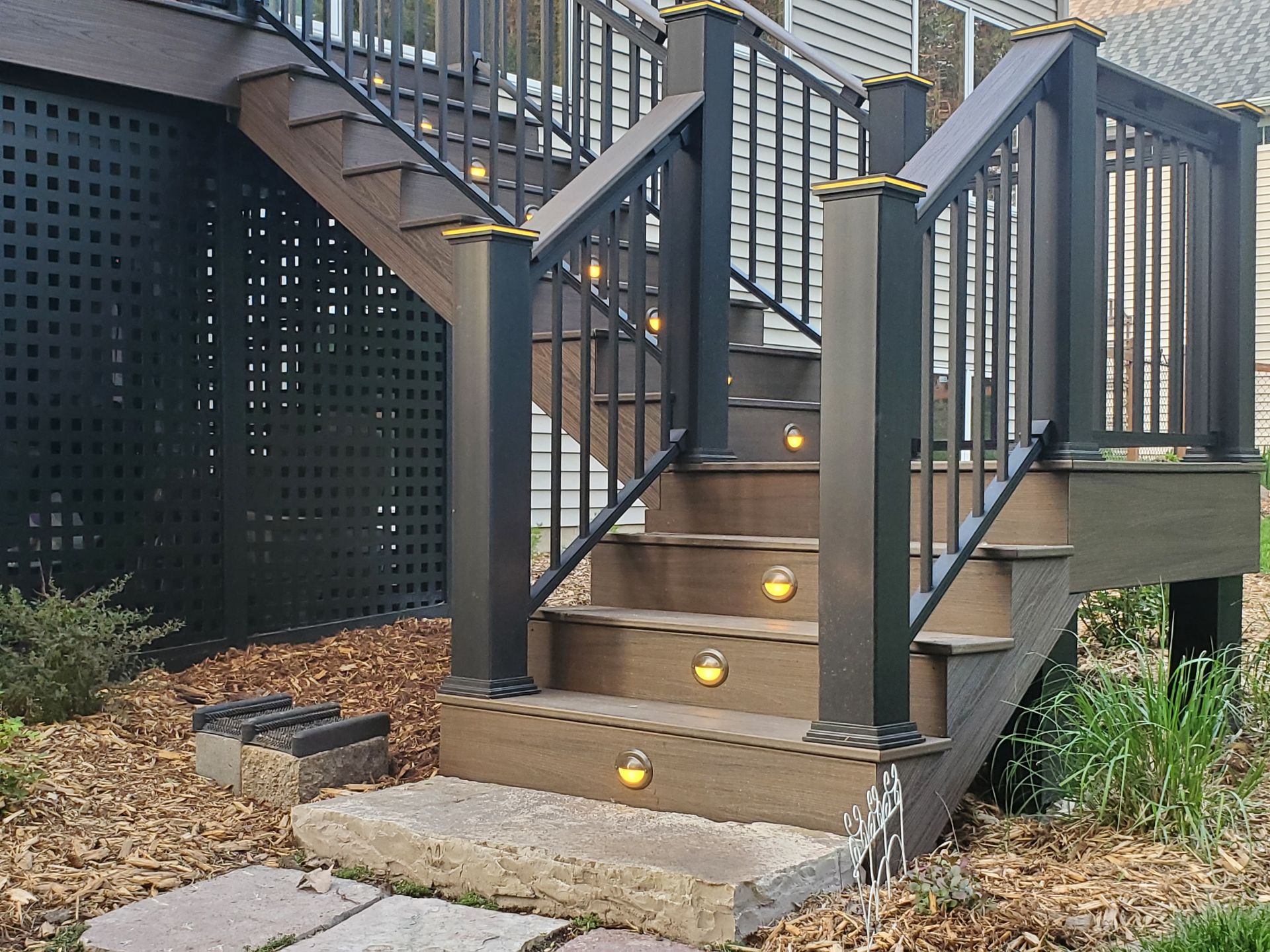 Outdoor deck stairs with brown composite steps and black railings featuring small, circular built-in accent lights.