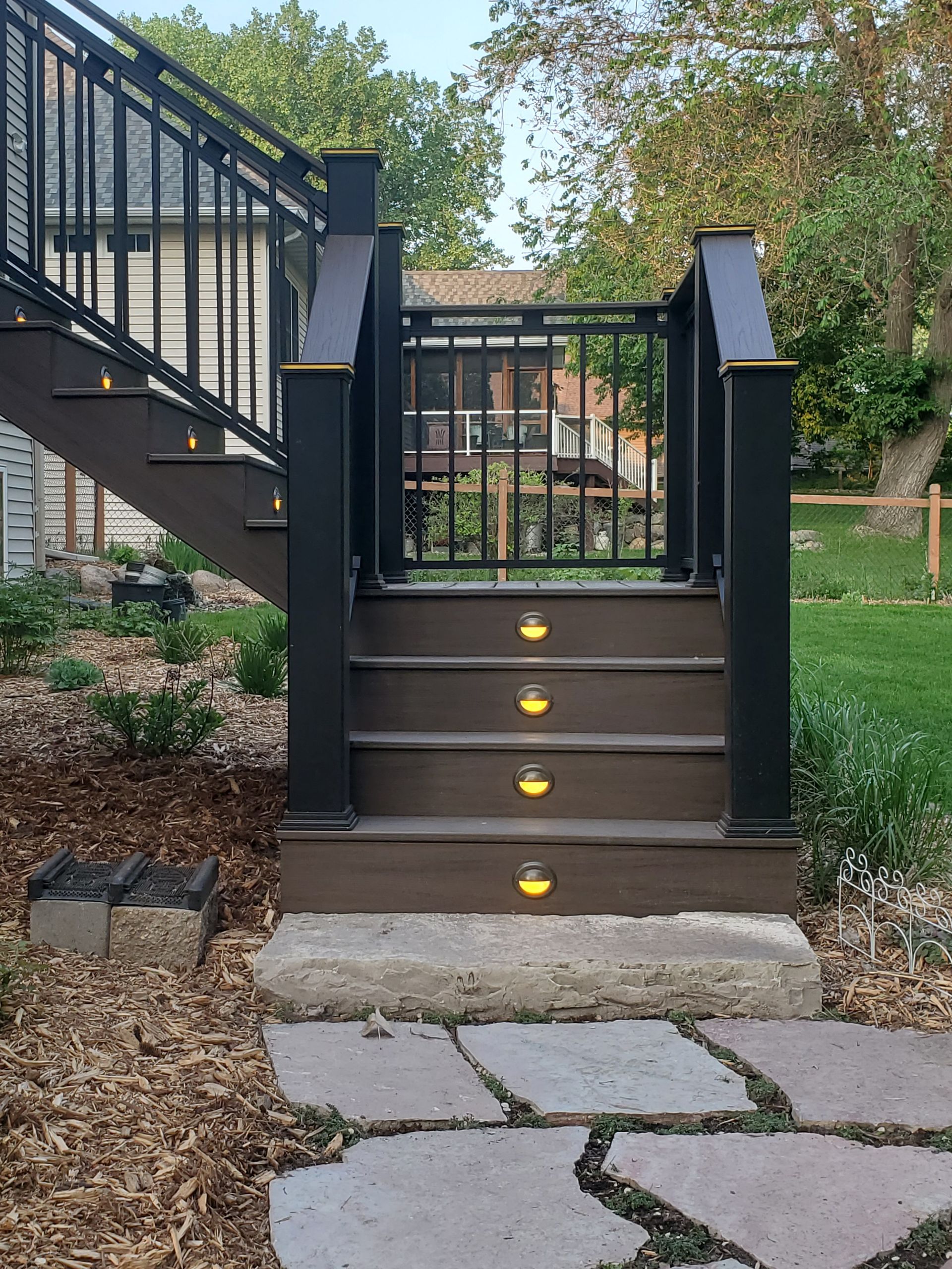 Outdoor wooden deck stairs with a safety gate, black railings, and small recessed lights on each step riser.