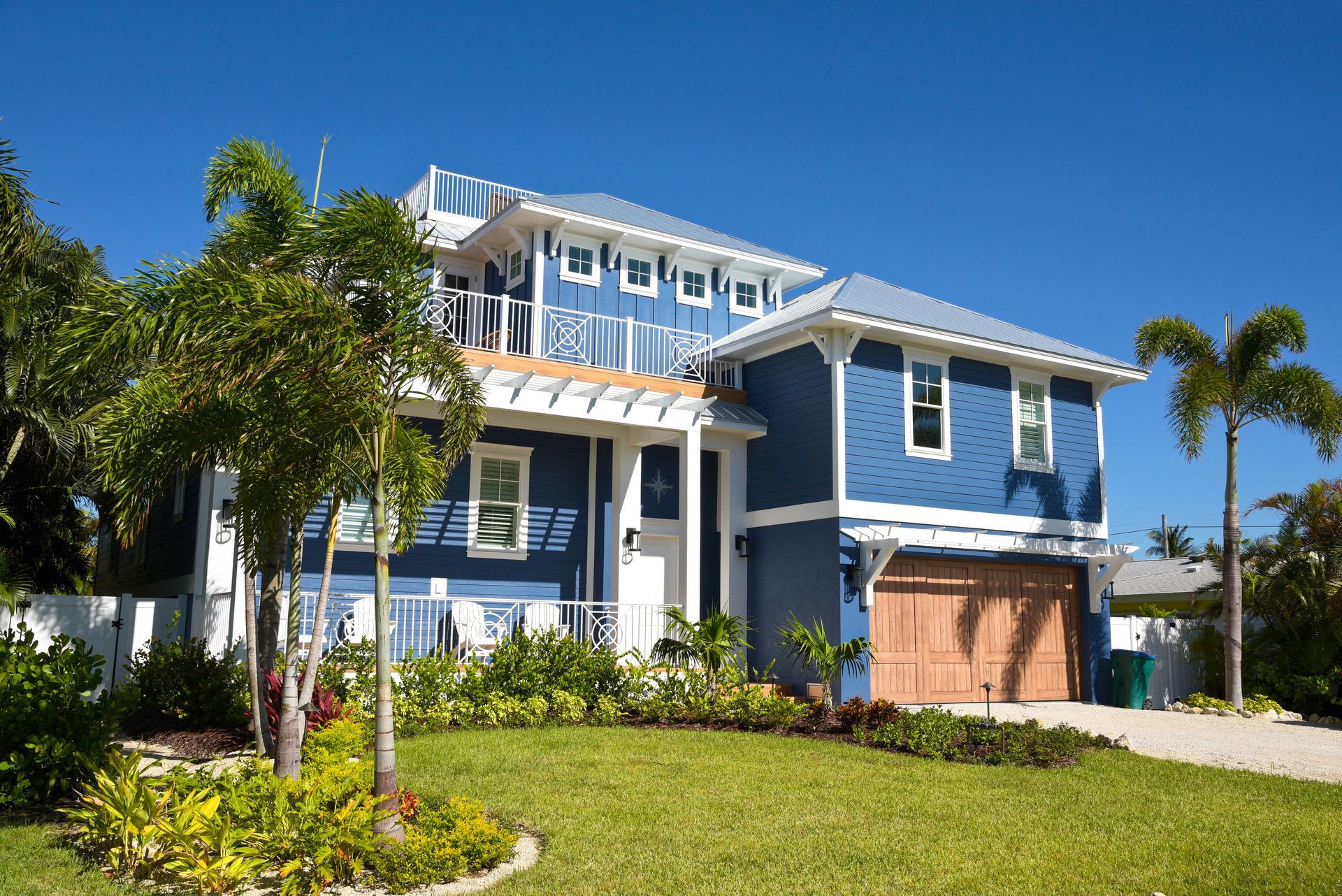 Blue and white coastal home with a green lawn and palm trees under a clear blue sky