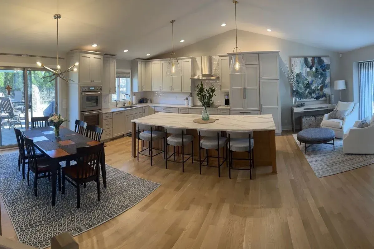 Open-plan kitchen and dining area with island seating, pale cabinets, and a long dining table.