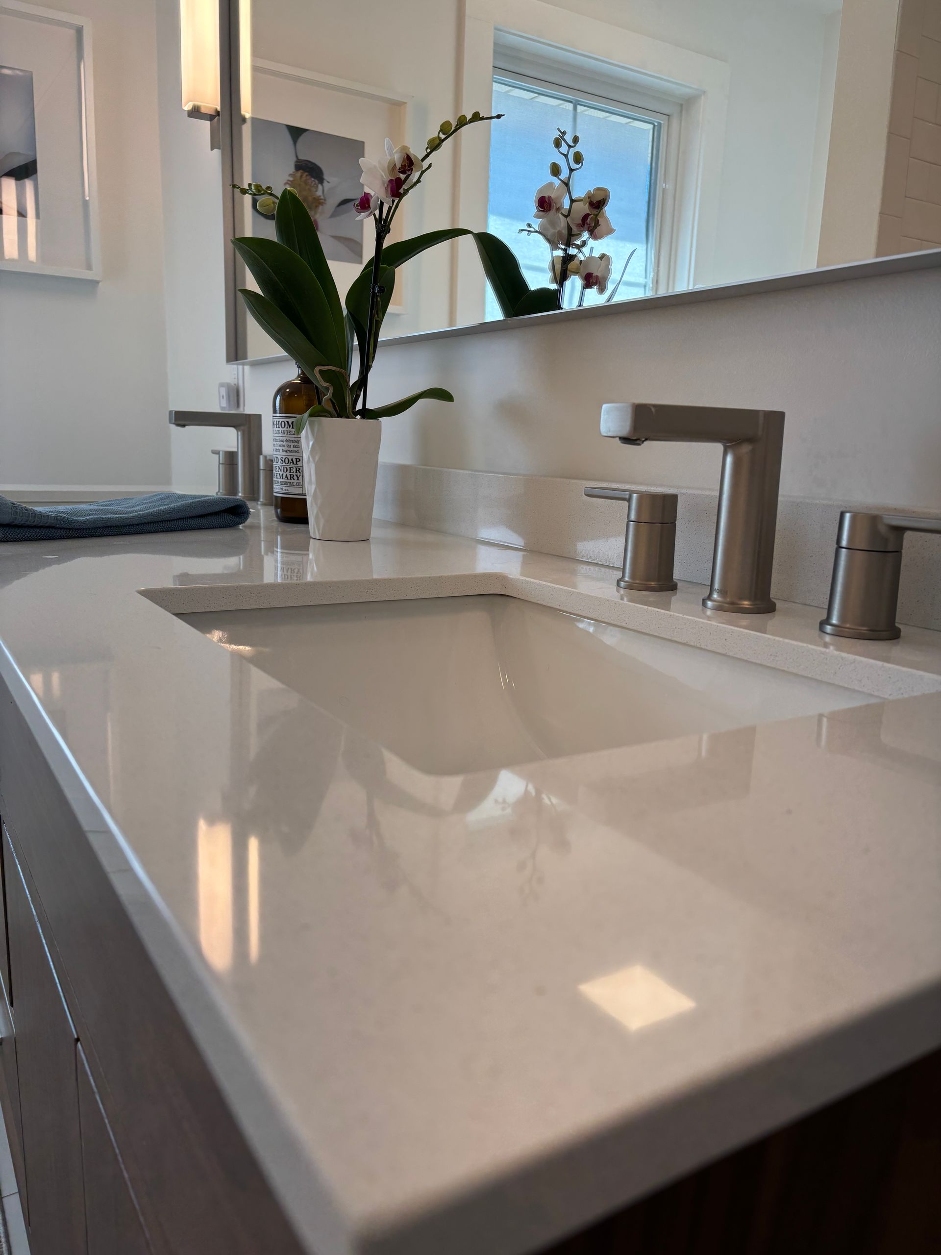 Modern bathroom with a white countertop, sink, and brushed nickel fixtures. An orchid sits on the counter.