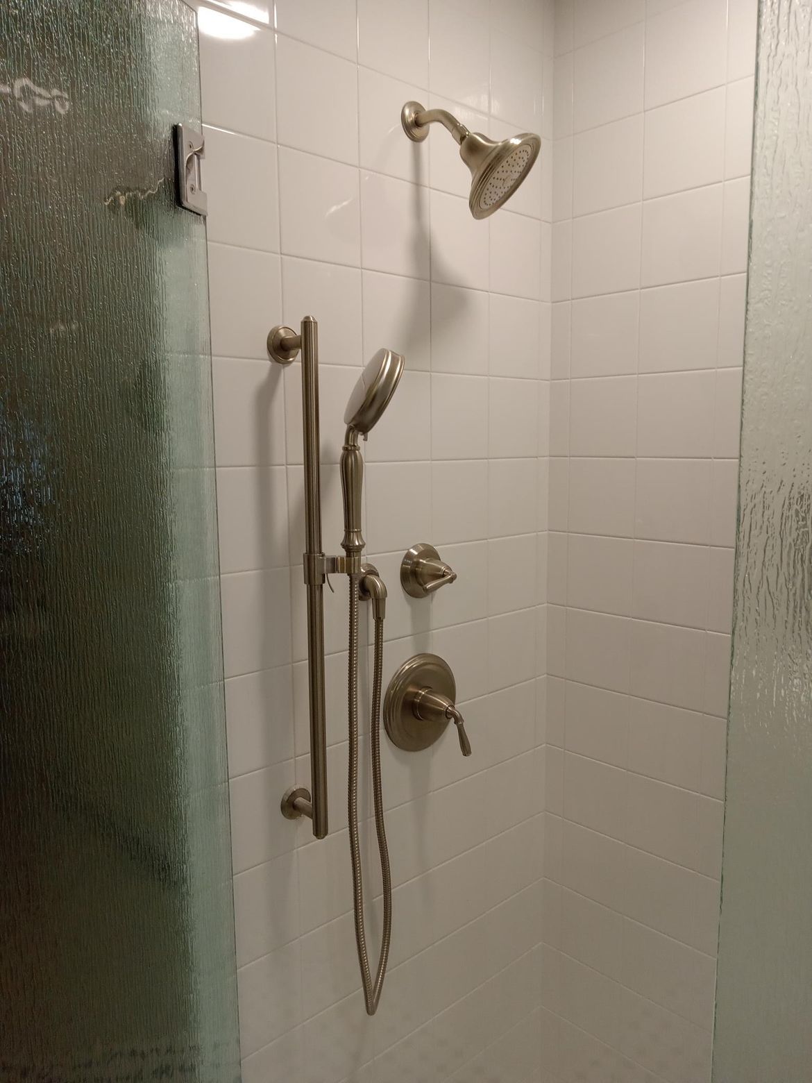 Shower with a handheld showerhead and a fixed showerhead on white tiled wall.