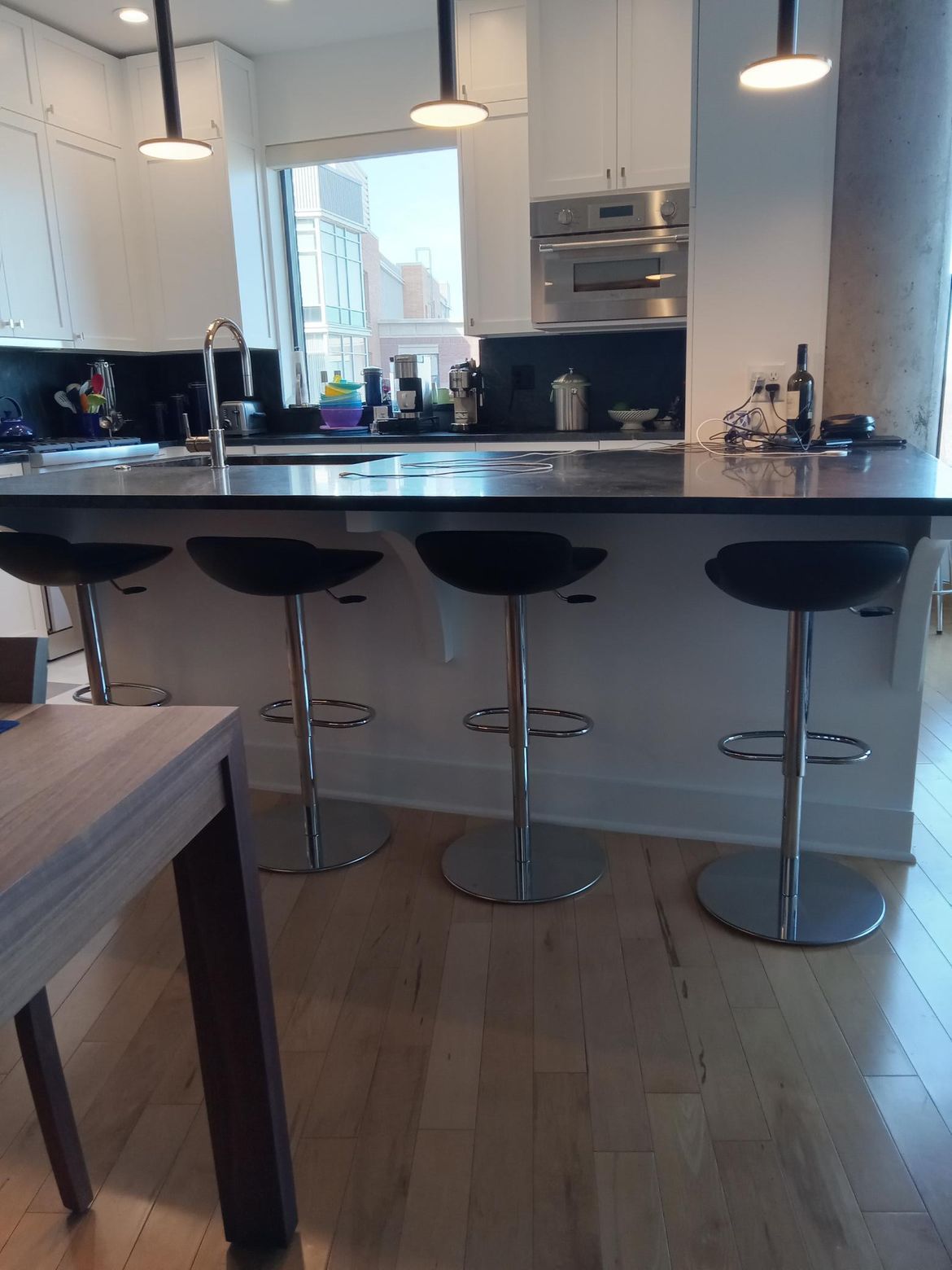 Kitchen with island, black countertop, four bar stools, and overhead lighting. Wooden floor.