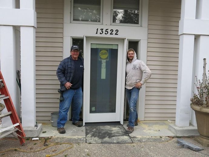 Two men stand in an open doorway of a building with the address