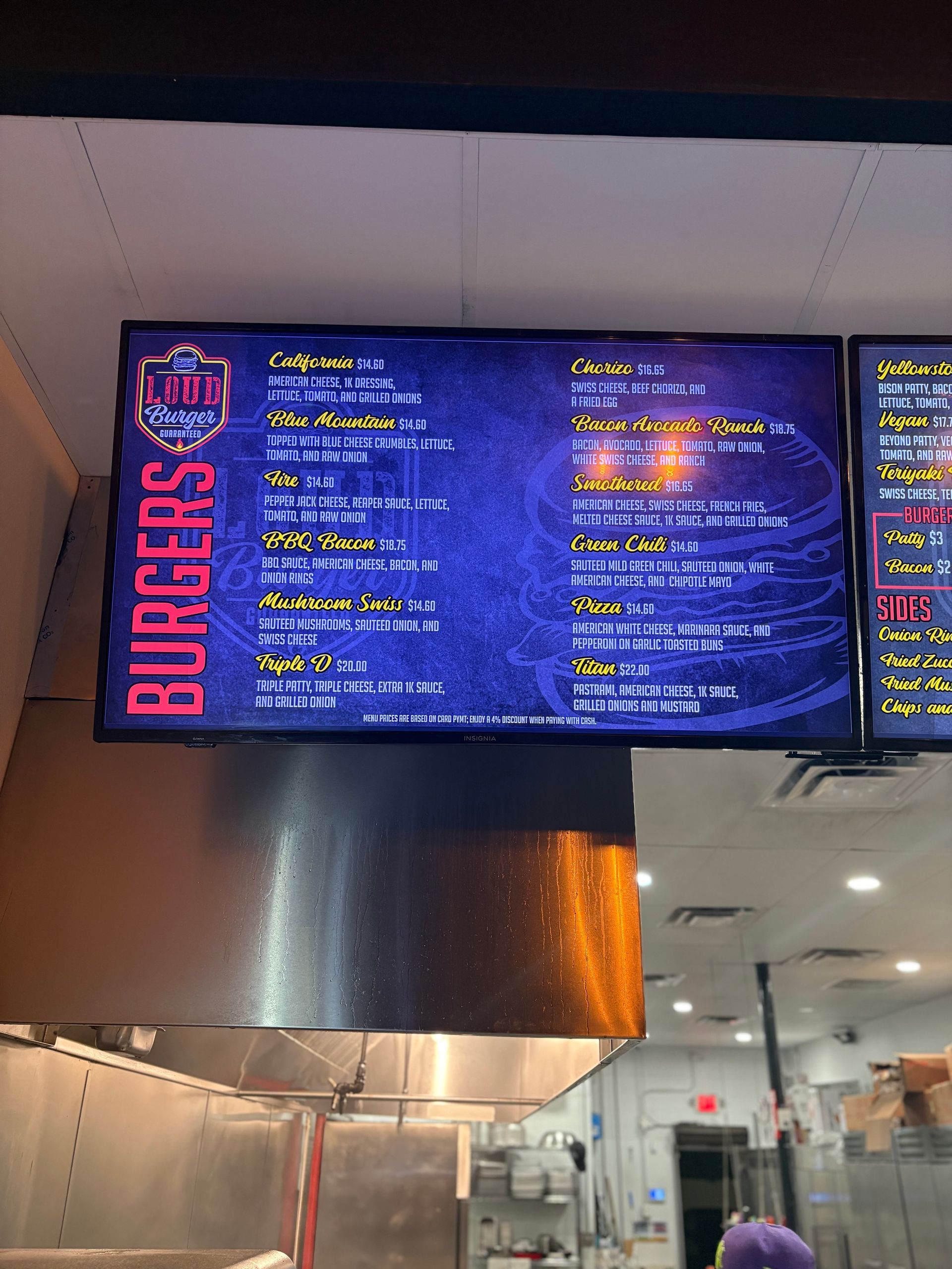 Digital menu board displaying burger options in a restaurant kitchen. The sign is black and blue.