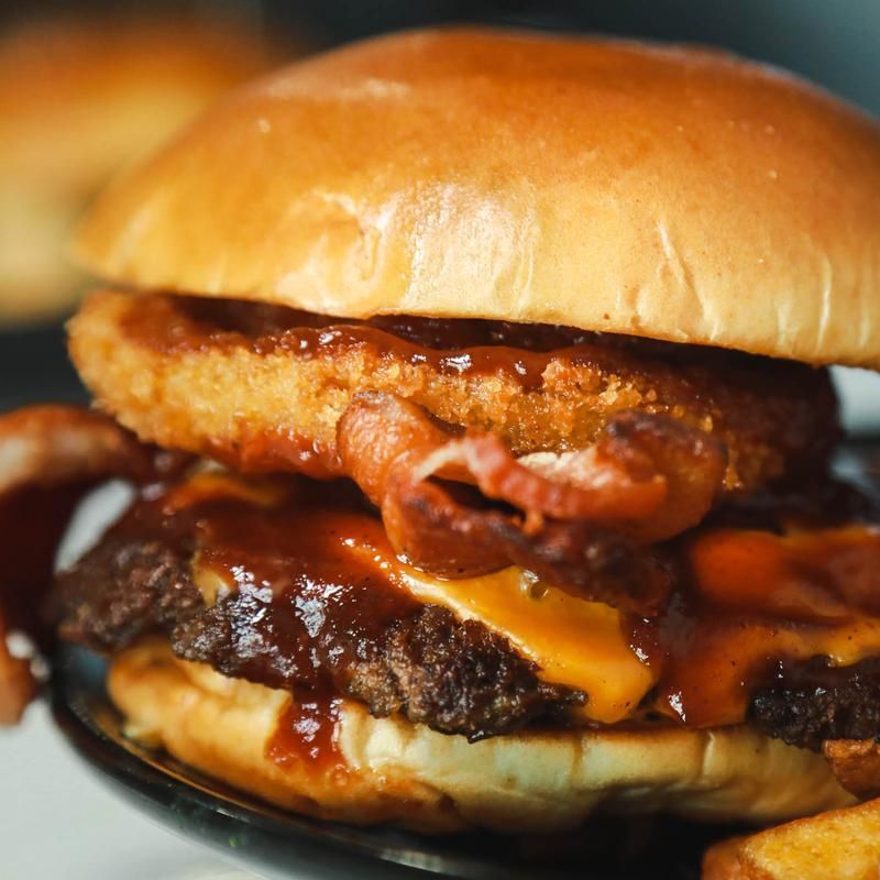 Burger with bun, patty, cheese, onion ring, bacon, and BBQ sauce.
