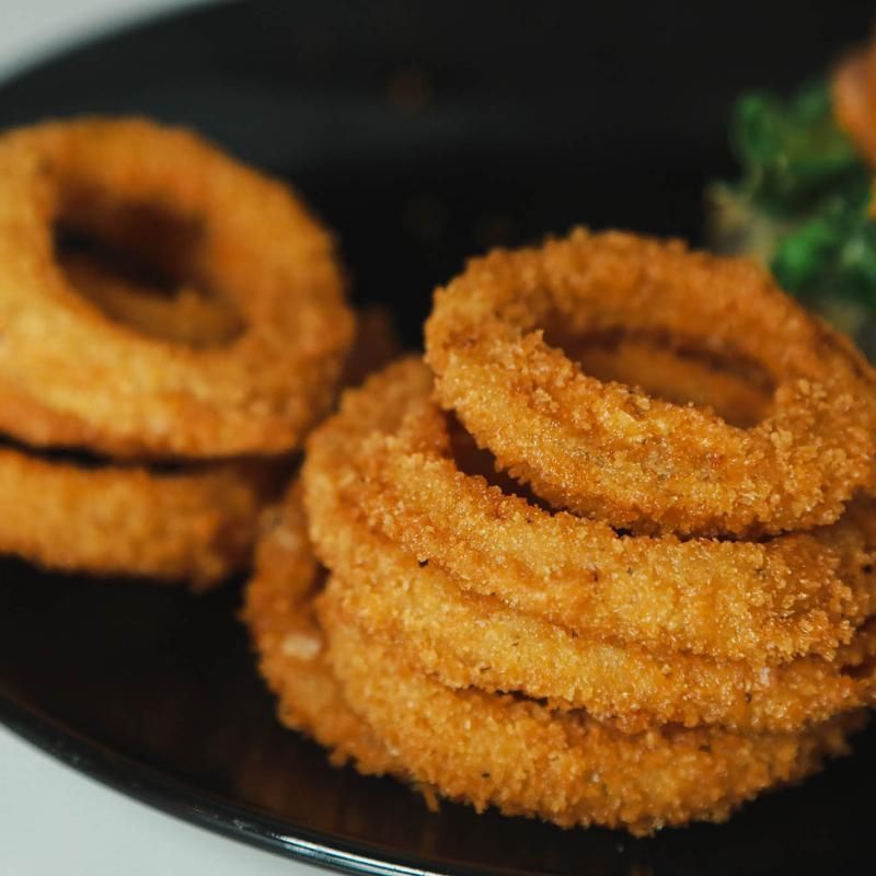 Crispy golden onion rings stacked on a black plate, some slightly blurred in background.