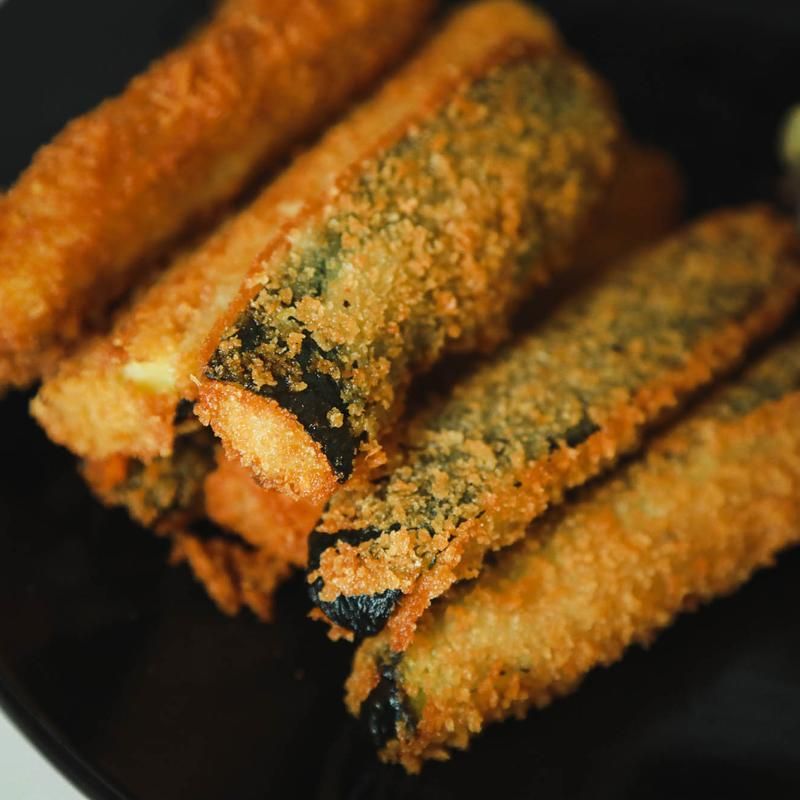 Fried zucchini sticks on a black plate, golden-brown breading, dark green zucchini.