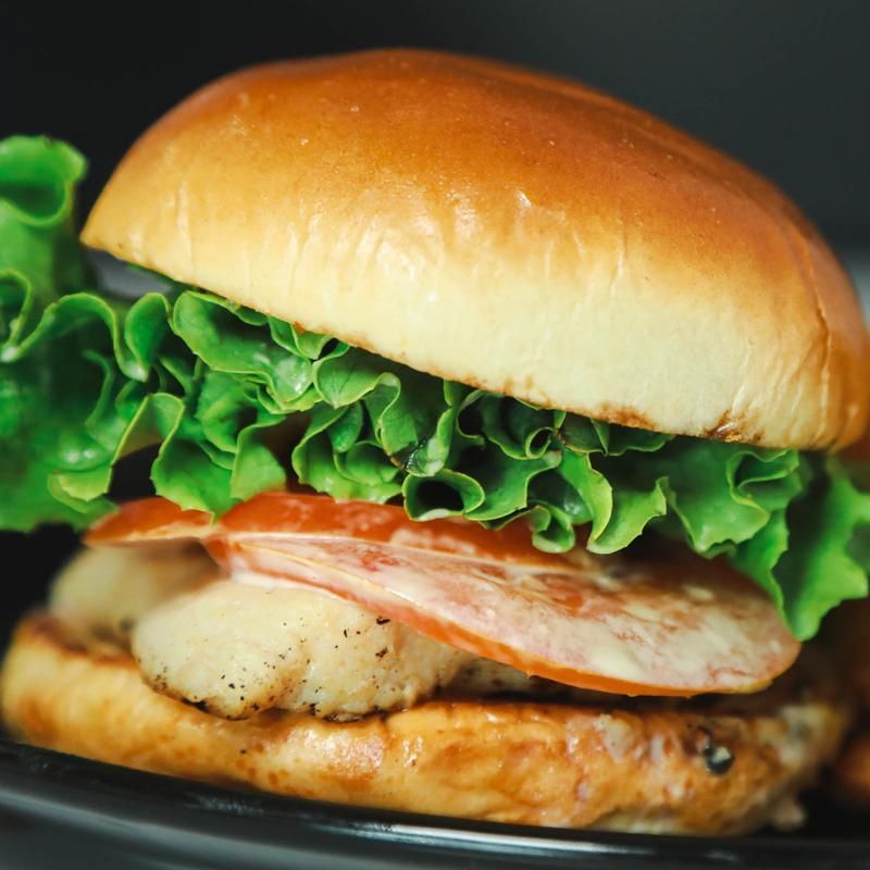 Burger on a bun with lettuce, tomato, and a white, cooked patty on a black plate.