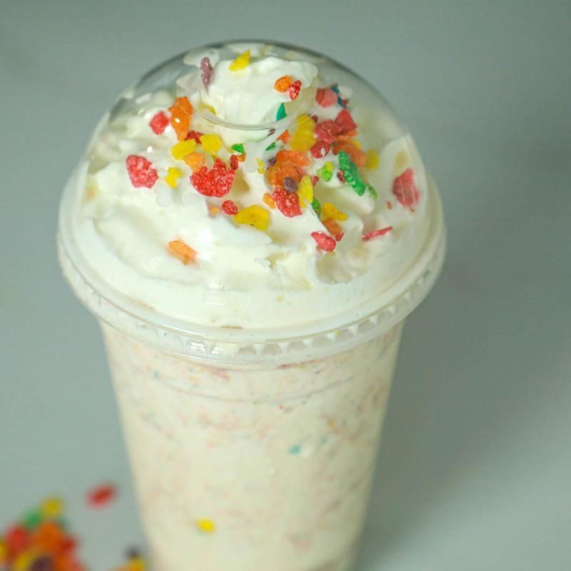 Whipped cream shake topped with colorful cereal in a clear plastic cup.