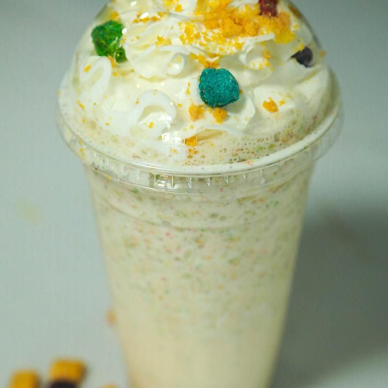 A milkshake in a clear plastic cup, topped with whipped cream and colorful sprinkles.