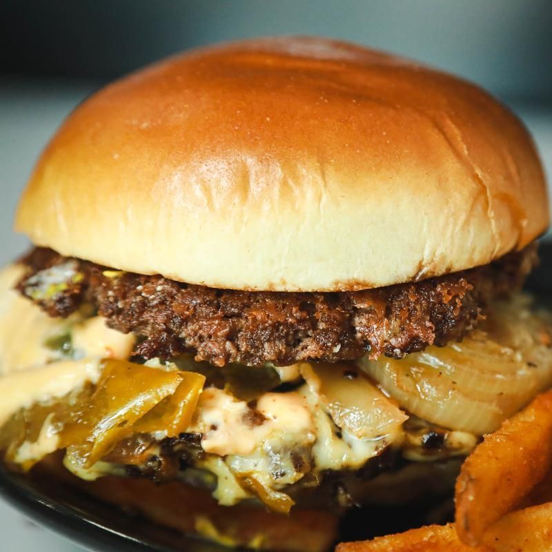 Burger with a toasted bun, patty, cheese, jalapeños, and onions, served with fries.