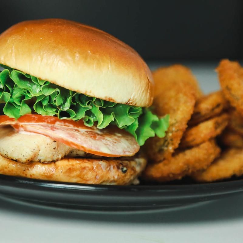 Burger with lettuce, tomato, and fried side. Black plate.