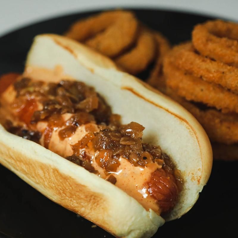 Hot dog with caramelized onions and onion rings on a black plate.