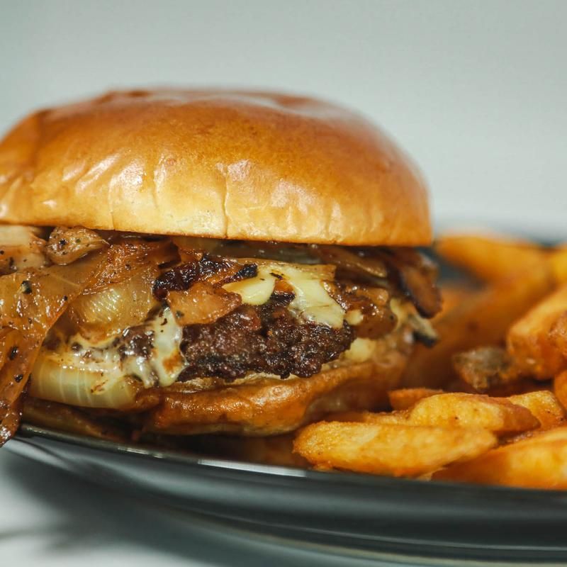 Cheeseburger with caramelized onions, and fries on a black plate.