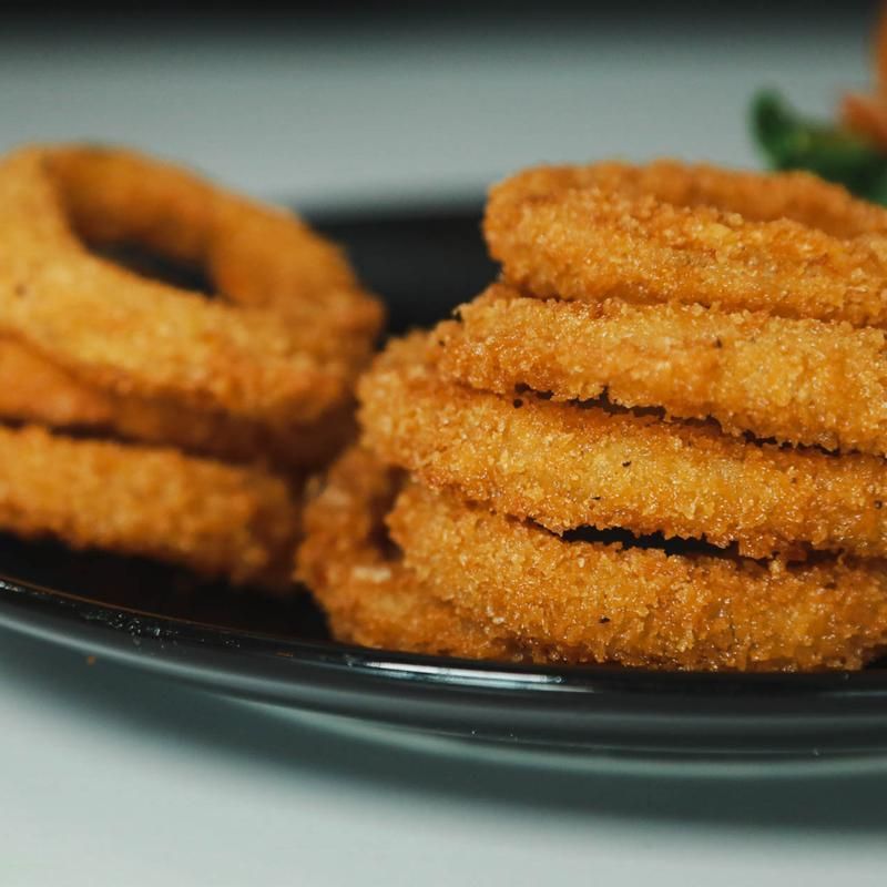 Close-up of golden fried onion rings stacked on a black plate.