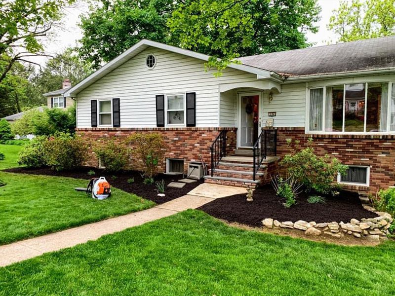 A white house with a brick side and a lush green lawn.