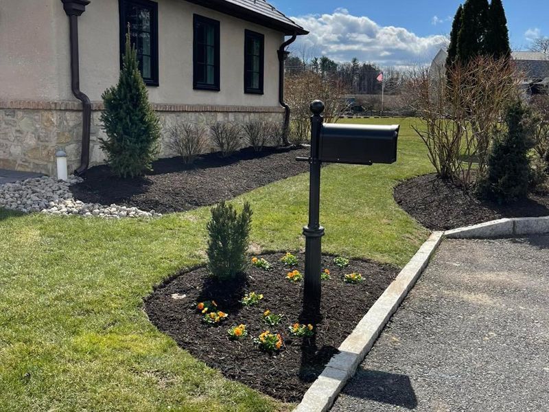 A mailbox is in the middle of a lush green yard in front of a house.
