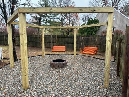 A wooden gazebo with a fire pit and swings in a backyard.