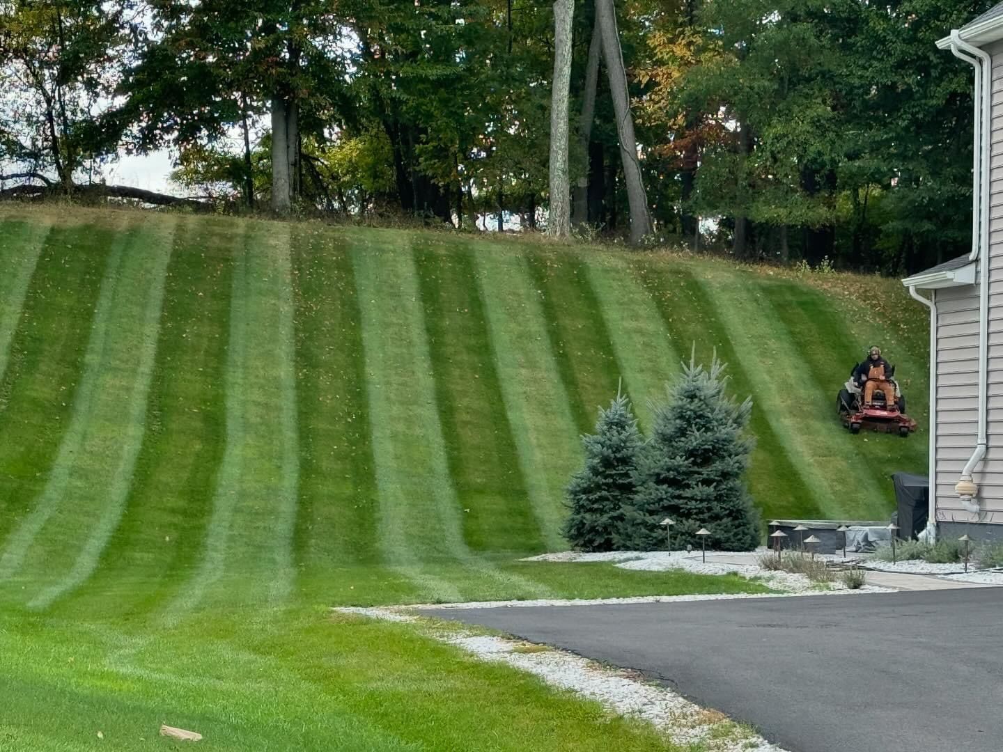 A lawn mower is cutting a lush green lawn in front of a house.