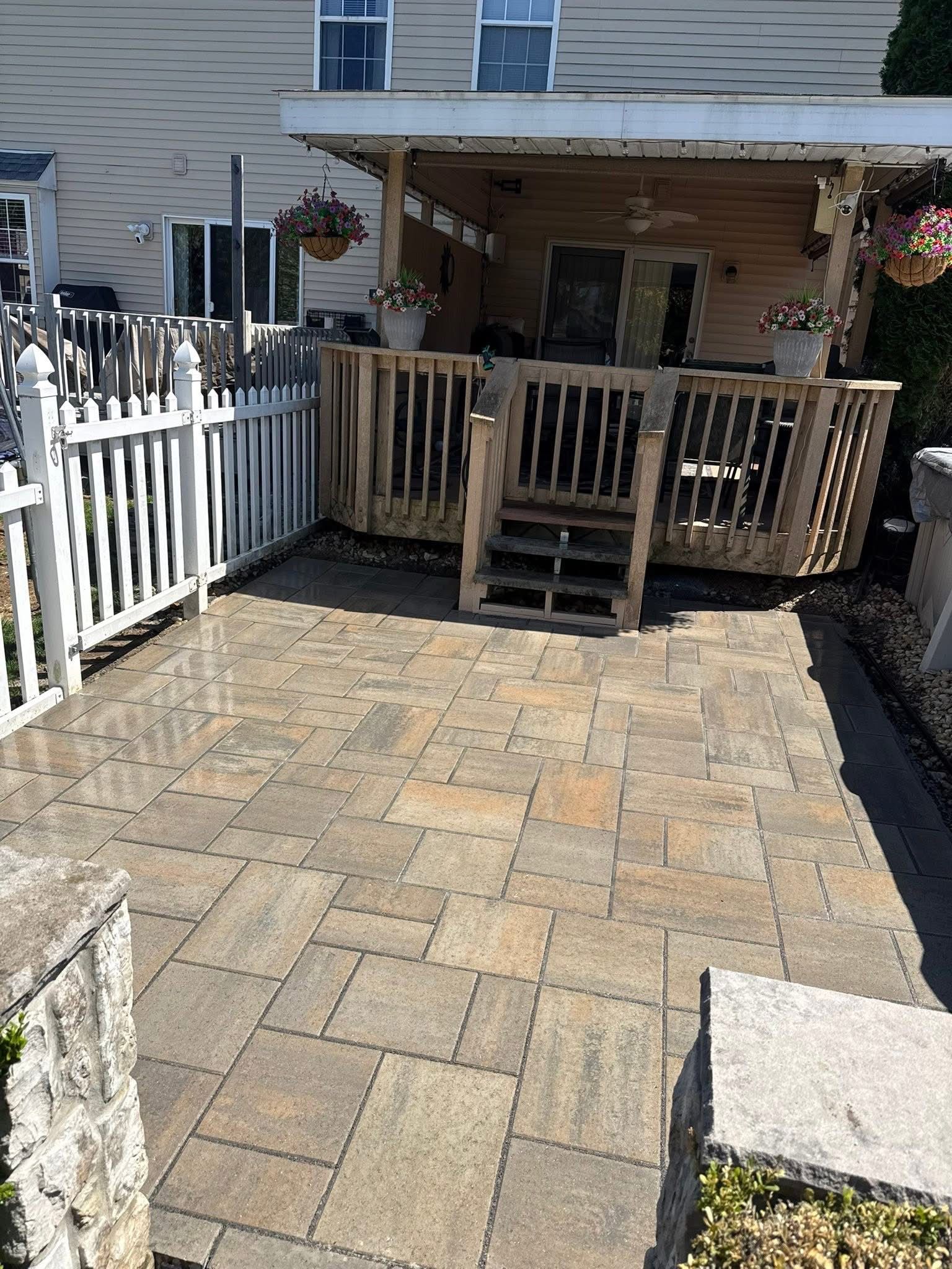 Stone patio leading to a small wooden porch with steps, white picket fence, and hanging plants.