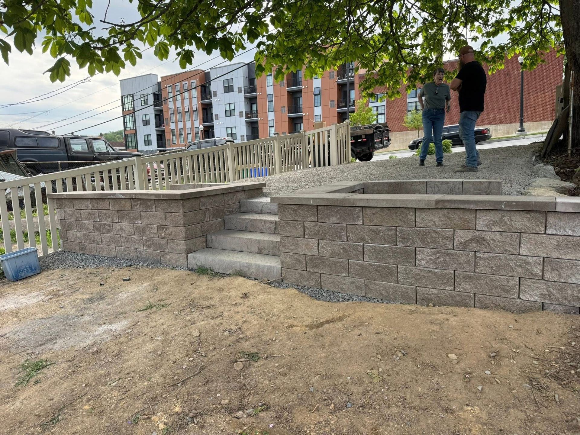 Accessible walkway and steps beside a brick retaining wall, with two people standing near a ramp under trees.