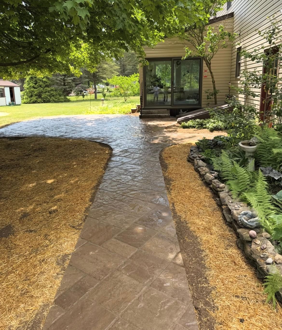 Stone walkway beside a landscaped yard and house, curving toward a glass sunroom.