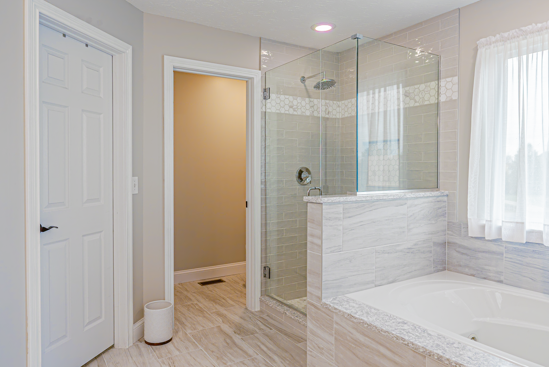 Bathroom with a glass shower, white bathtub, and white door.