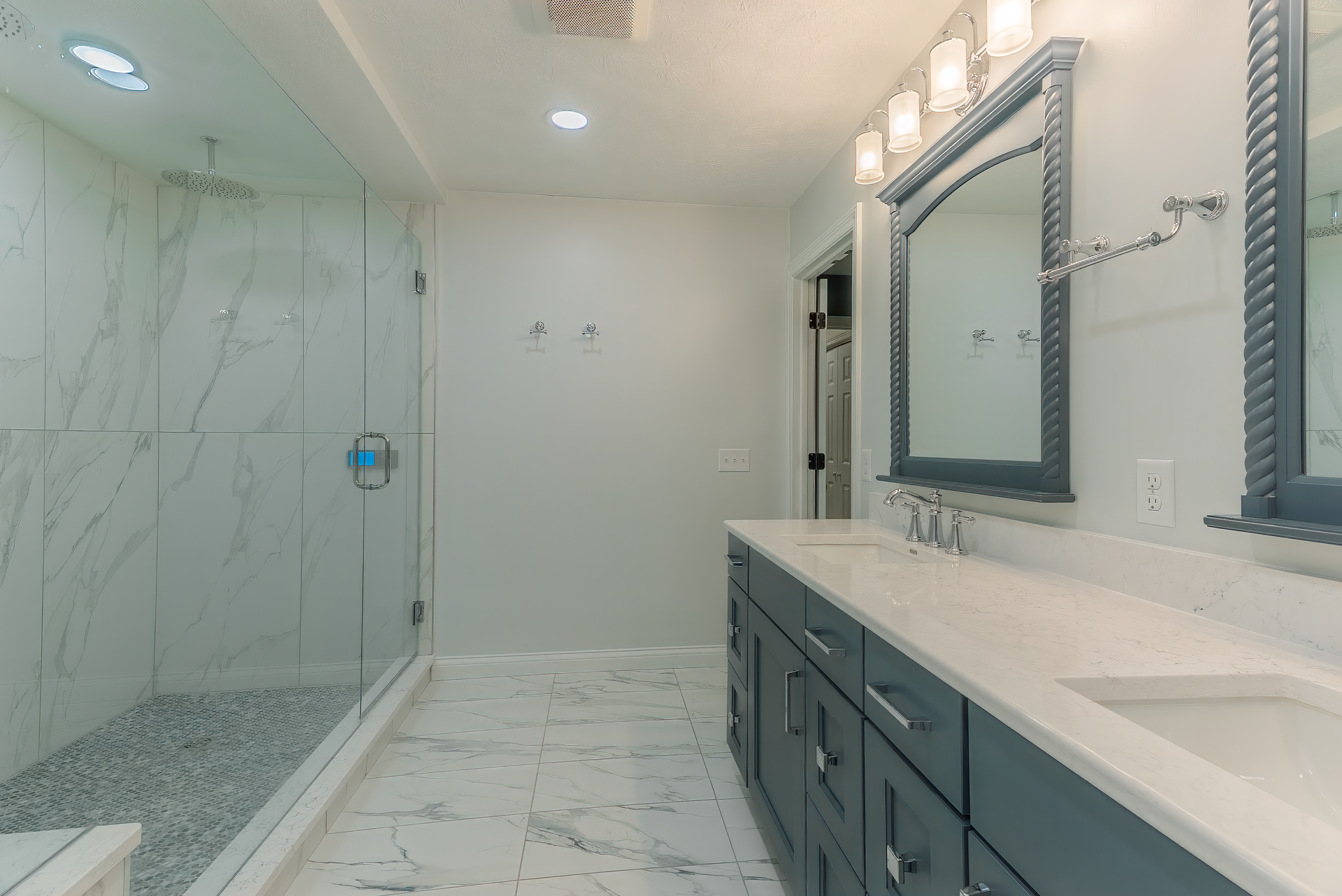 Spacious modern bathroom with a glass shower, double vanity, and marble-look tile floors.