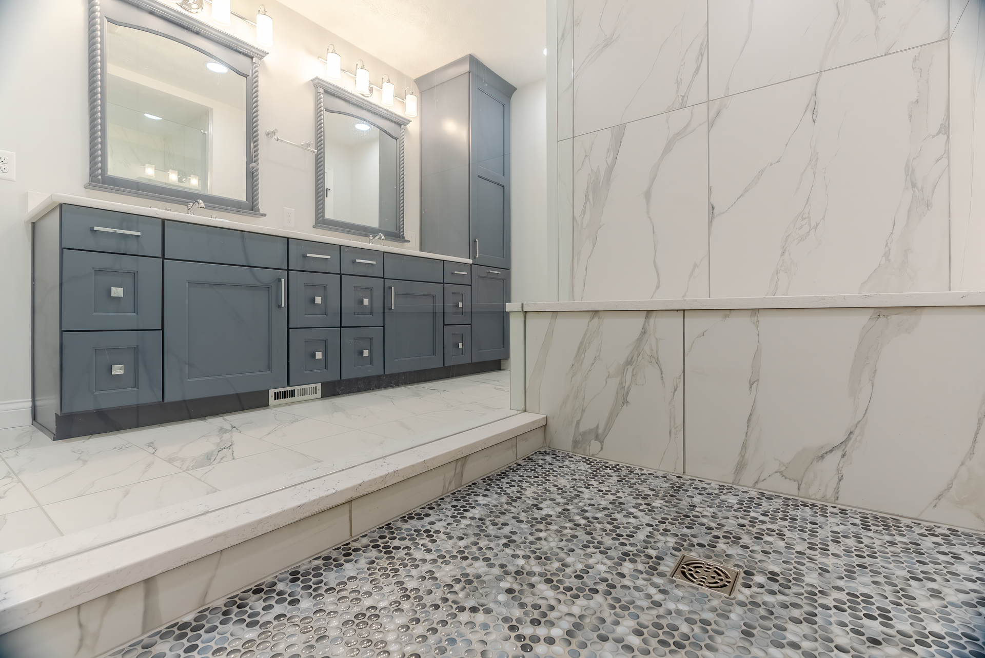 Modern bathroom with blue vanity, marble tile, and pebble shower floor.