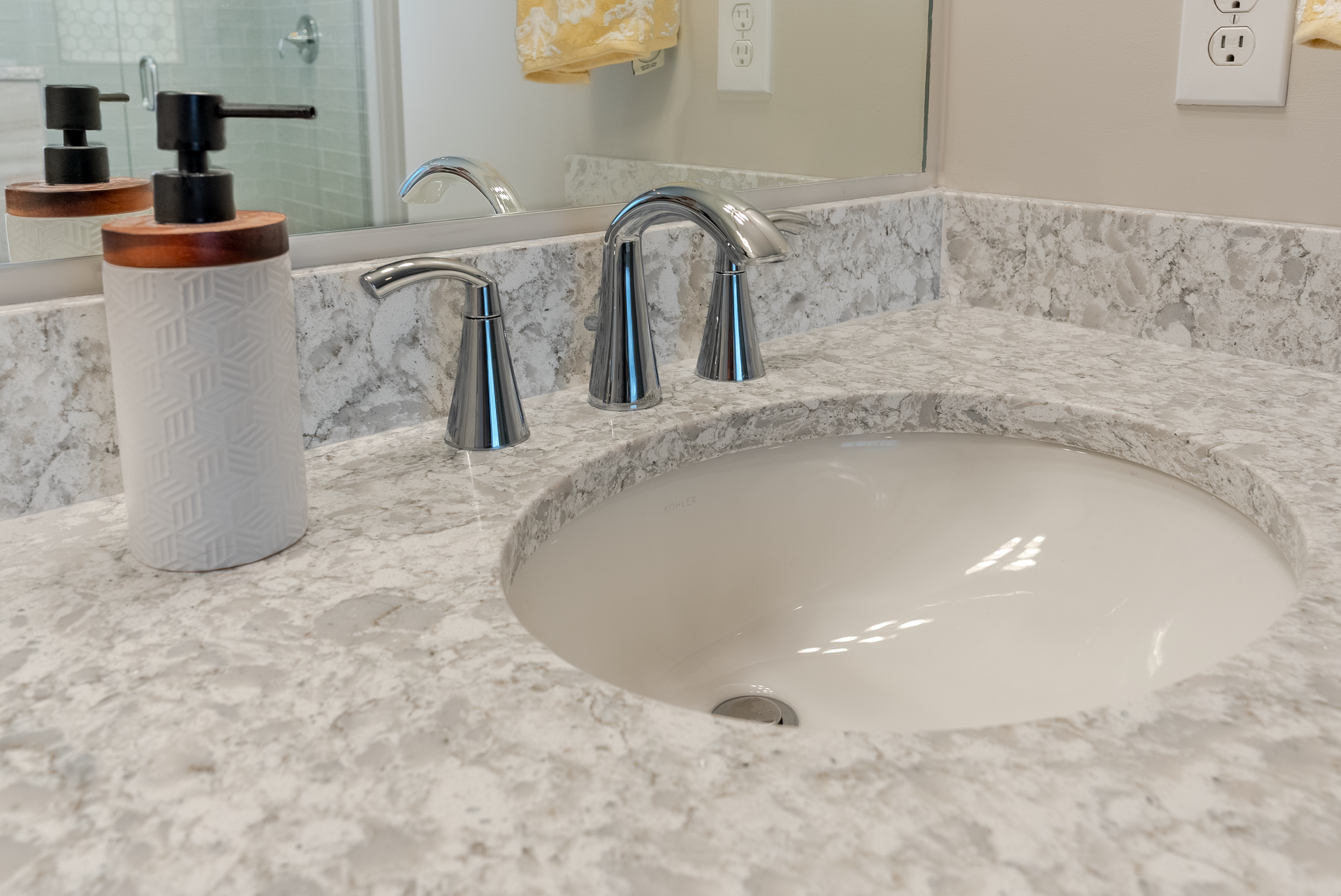 Bathroom sink with a white oval basin, chrome faucet, and soap dispenser on a gray and white countertop.