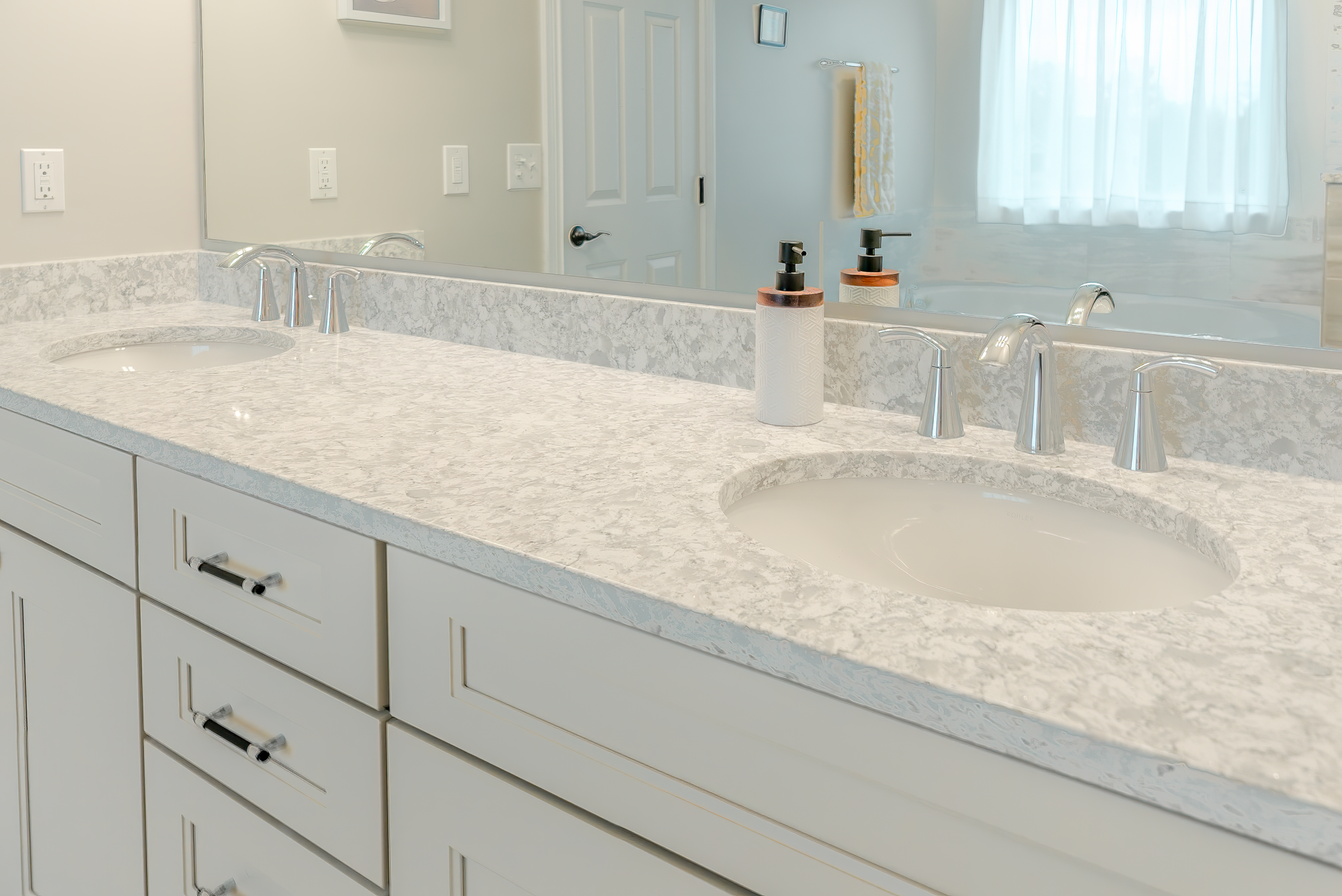 White bathroom vanity with two sinks and countertop, large mirror, and window.