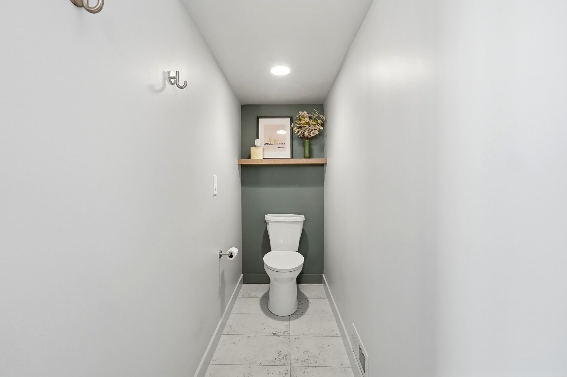 Narrow bathroom with white walls, a toilet, shelf with decor, and a teal accent wall.