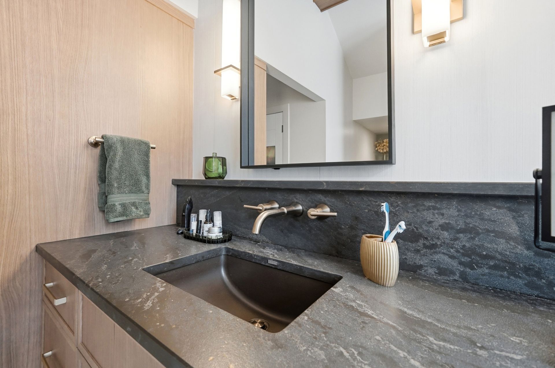 Bathroom vanity with dark countertop, built-in sink, and wall-mounted faucet. Includes a mirror and towel rack.