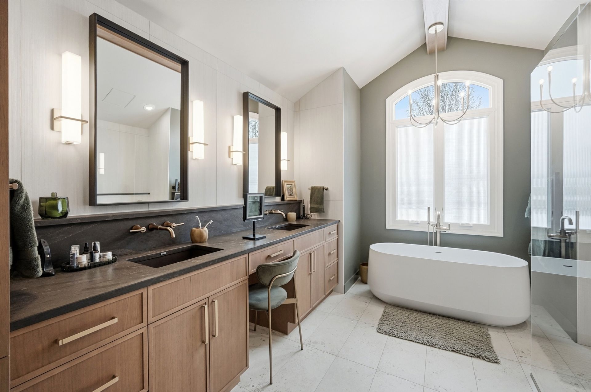 Bathroom with wooden cabinets, dark countertops, two mirrors, a bathtub, and a large window.