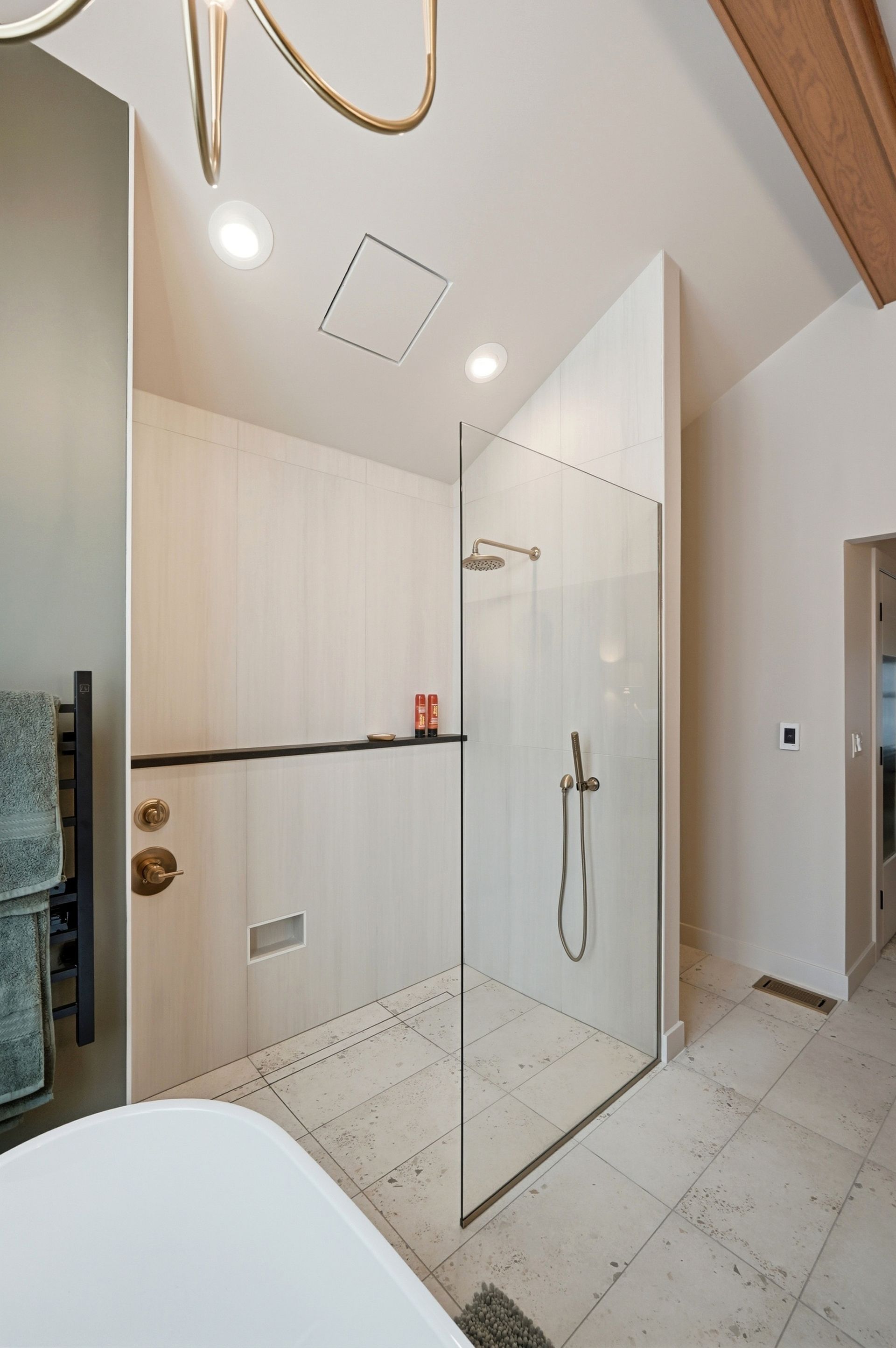 Modern shower stall with glass door, tiled floor, and light-colored walls. A towel rack is on the left.